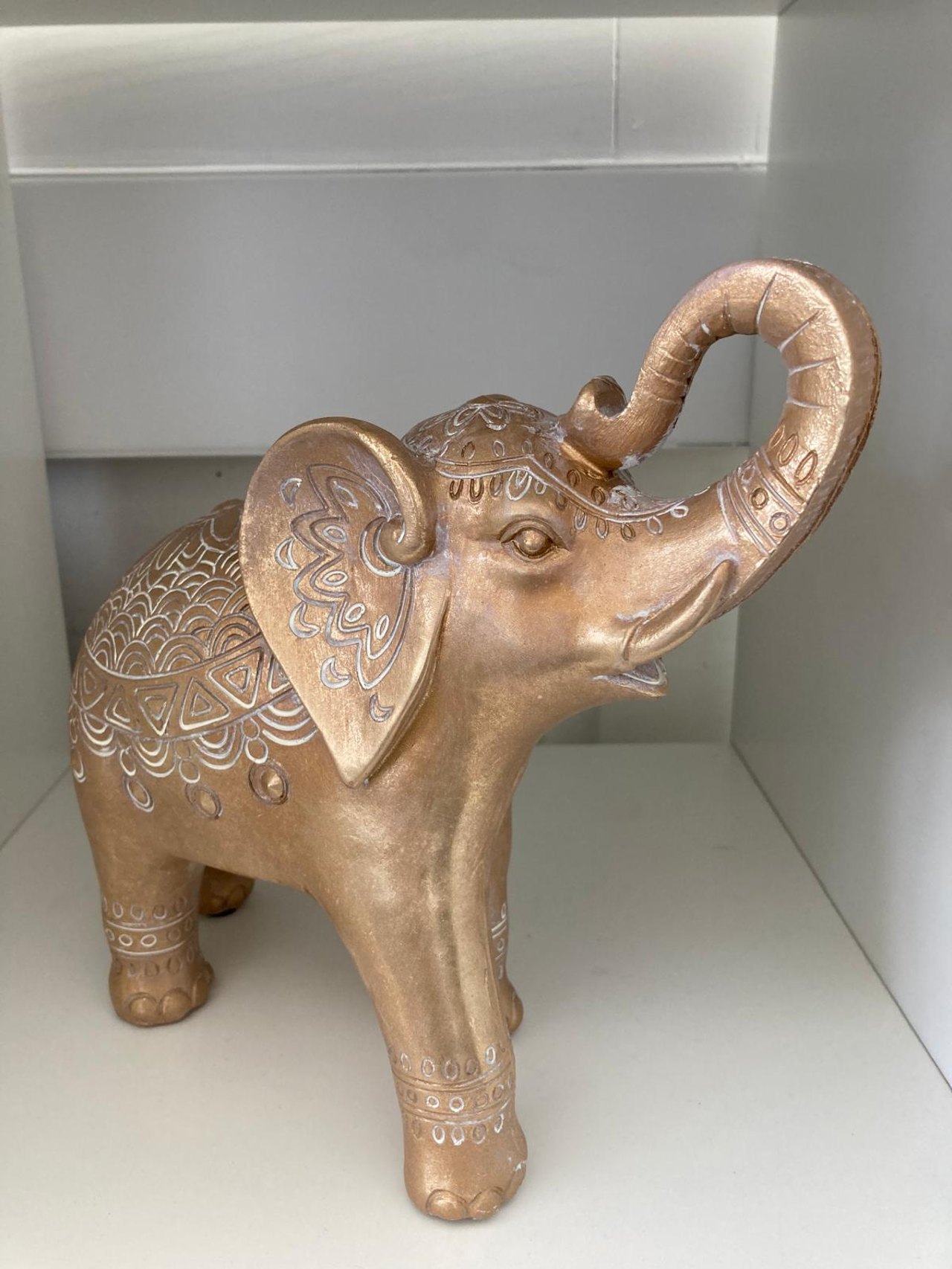 Goldfarbene Elefantenfigur mit erhobenem Rüssel und weißen Ziermustern auf dem Rücken und den Ohren.